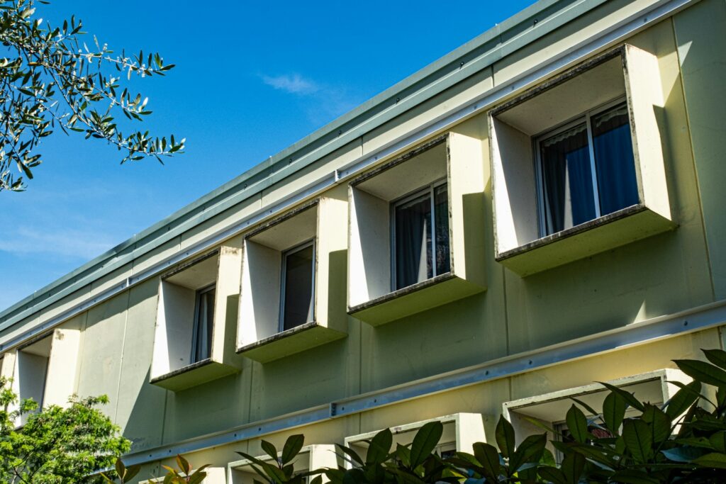 Light green building with deep projecting window reveals that cast shadows to shade the rooms