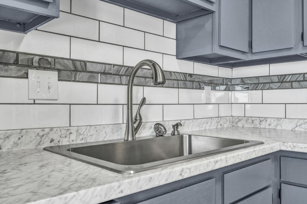 Stainless steel kitchen sink with a gooseneck tap and white tiled wall